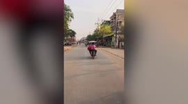 Talented female rider balances food tray on head while riding in Cambodia