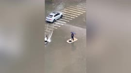 Elderly Chinese man stands on foam board to paddle along flooded road