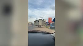 Cambodian man carries his wooden hut along road on trailer