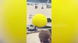 Performer wearing giant yellow balloon entertains beachgoers in Korea