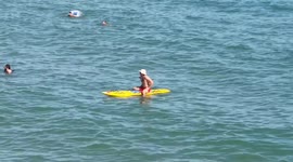 Buff lifeguard on surfboard at sunny Bournemouth beach patrols the seaside resort