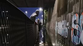Two teenage boys attempt to cross floodwater on the A406 in South Woodford by climbing across a fence.