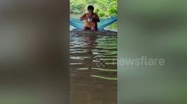 Woman stranded in floods plays in water with her pet dog while feeding fish