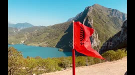 Waving Albanian flag with the Bovilla mountainous lake view in the background