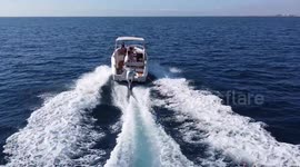 Goup of friend water skiing over inflatable donut pulled by motorboat. Aerial view from drone.