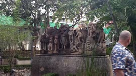 Haughty stray cat ignores amused tourists as it relaxes on top of statues in Thai park