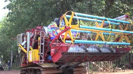 A large rice harvesting machine is loaded onto a tow truck, on a small rural road in Thailand.
