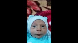 Wide-eyed new-born baby tries to avoid looking at the camera