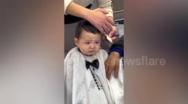 Nervous toddler bravely holds back the tears as he gets a haircut for the first time
