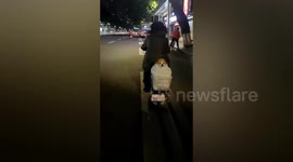 Dog on back of scooter beats the cold by being tightly wrapped in blankets