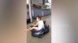 Amused resident drifts down flooded street on inflatable toy in Thailand