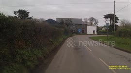 A Quad being driven on a fairly narrow Cornish road with A CHILD  sat on the lap of an adult