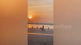 Chinese man dances with arms while cycling on lakeside square