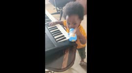 Baby playing piano with bottle of juice