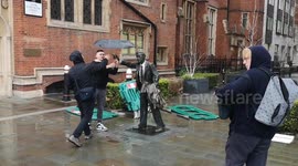 Tourists have fun in the wind and rain with a statue near Blackfriars Underground Station