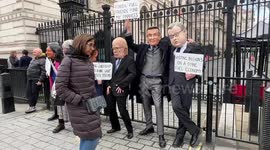 Big heads of various MPs stand outside Downing Street gates