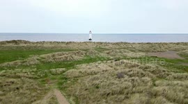 Drone floating towards and away from a lighthouse on a sandy beach