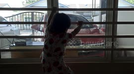Excited one-year-old climbing up windows enclosure when sees her brother back from school