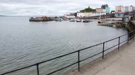 Tenby Harbour at high tide with boats in mooring and sails raised with colourful pastel coloured homes surrounding the bay.