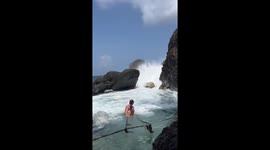 Waves Crash Into Swimmers Resting in Natural Pool