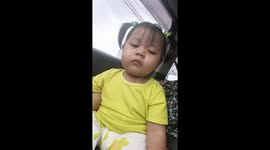 A small cute kid in a car is fighting to try to stay awake even though she is very tired