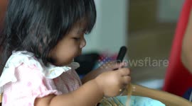 An adorable one year old girl learning to eat noodles and egg for the first time using a spoon.