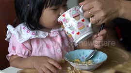 A very cute child who is only one year old is learning to eat a noodle breakfast by herself.