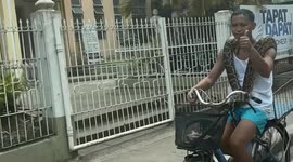 Cyclist rides down street with pet python wrapped around shoulders