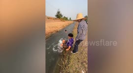 Locals ride flowing water in rice field irrigation as makeshift slip-and-slide