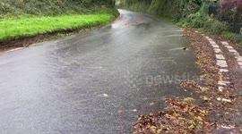 Vehicles driving through rainwater running off a field in Exeter, UK