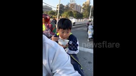 上学赶时间 男孩端着碗在家长后座干饭
