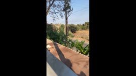 The video frames the enchanting view of Kolympia, Rhodes, from a higher vantage point, unveiling a panoramic spectacle of the village nestled against majestic mountains. The camera captures the idyllic coastline, quaint homes dotting the landscape, and lu