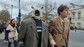 A man takes his robot dressed in a suit for a walk in London during London Fashion Week