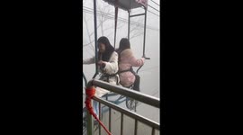 Two women pedal back-to-back on bicycle attached to cable wire