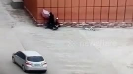 Man riding a scooter while holding an umbrella crashes into wall