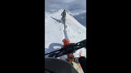 Two dirt bikes trudge trough deep snow on top of a mountain ridge