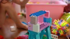 The video shows a child playing with plastic building blocks, assembling a structure. The child's hands are in focus, carefully placing a block onto a partially built creation.