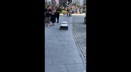 A small delivery robot traveling down a pedestrian sidewalk.