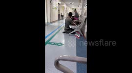 Touching scene as son knees down and lets sick mother rest head on his arms at Chinese hospital