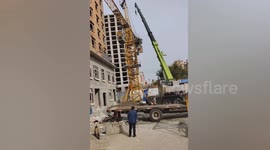 Overloaded crane topples over with workers clinging to base