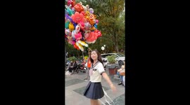 Thoughtful balloon seller crouches to give girl colourful selfie background
