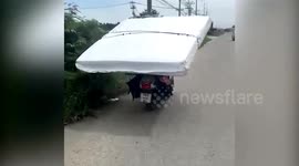 Deliveryman carries mattress on his HEAD as he rides to customer