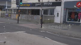 Storm Darragh, Pedestrians struggle against 80mph gusts, hoardings down, flying debris swirls, Cornwall, UK