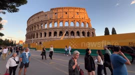 Tourists stroll through Colosseum Square with the Colosseum in the background illuminated by the warm light of sunset on a clear October Sunday in Rome.