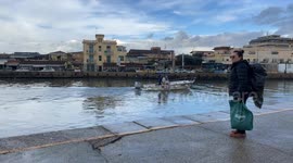 A traveler with a bag in her hand and a backpack on her back on the dock while a boat sails up the canal port in Fiumicino.