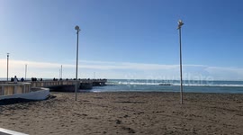 A stretch of beach at Lido di Ostia with the Pontile di Ostia in the background and a calm sea on a clear December day in Rome.
