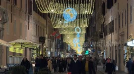 People walking in the evening on Via del Corso and above their heads the lights installed during the Christmas period in Rome.