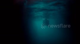 Underwater diving at cave or cavern silhouette of muscled man swimming undersea with low light.