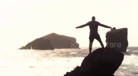Man silhouette standing on rock with open arms against monsteiros beach in Sao Miguel, Azores Island.