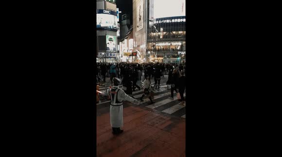 Busy Shibuya Crossing in Tokyo by night. A policeman guiding and overseeing the traffic flow.